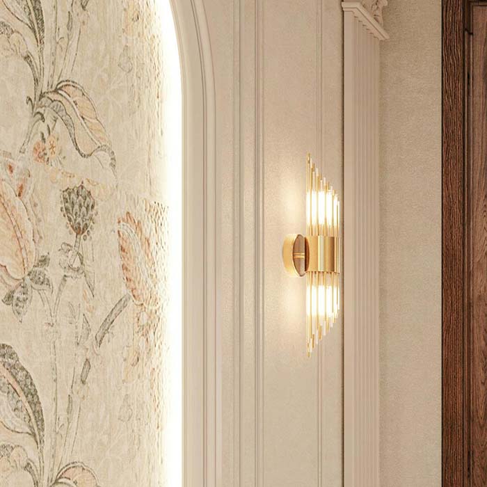 A gold-toned cylindrical wall sconce mounted on a softly patterned surface, providing warm, localized lighting.