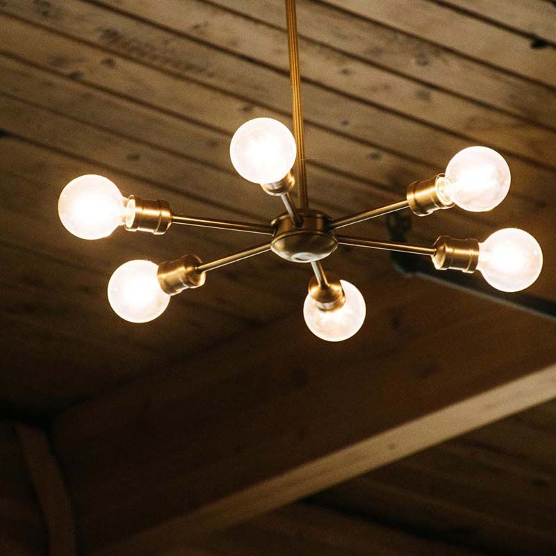 Brass chandelier featuring multiple spherical bulbs, suspended from a wooden ceiling in a cozy interior.